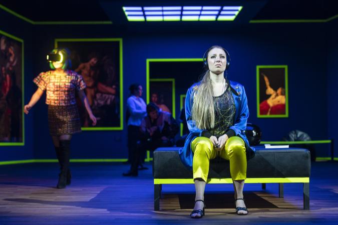 Szene auf einer Theaterbühne: Frau mit Kopfhörern sitzt in Kunstmuseum auf einer Bank