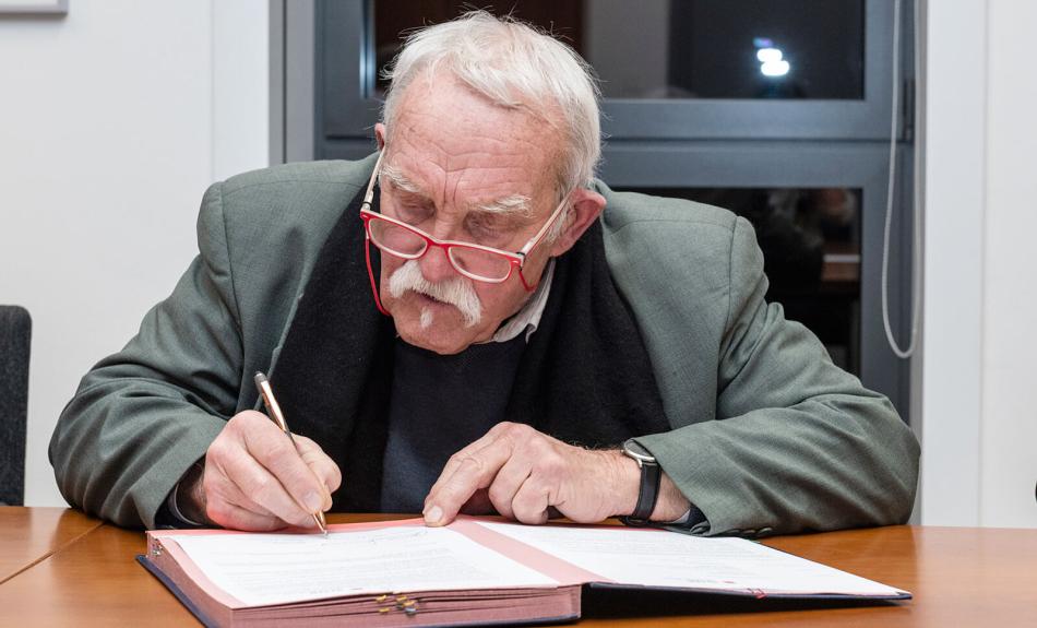 Älterer Herr an Tisch sitzend unterzeichnet Vertrag