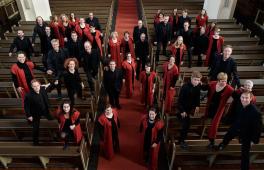 Chor in schwarzer und roter Kleidung steht in einem Kirchenschiff verteilt