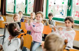 Kinder spielen gemeinsam im JeKits-Orchester auf ihren Instrumenten. Im Vordergrund des Fotos sind drei Mädchen mit ihren Kinder-Querflörten zu sehen.