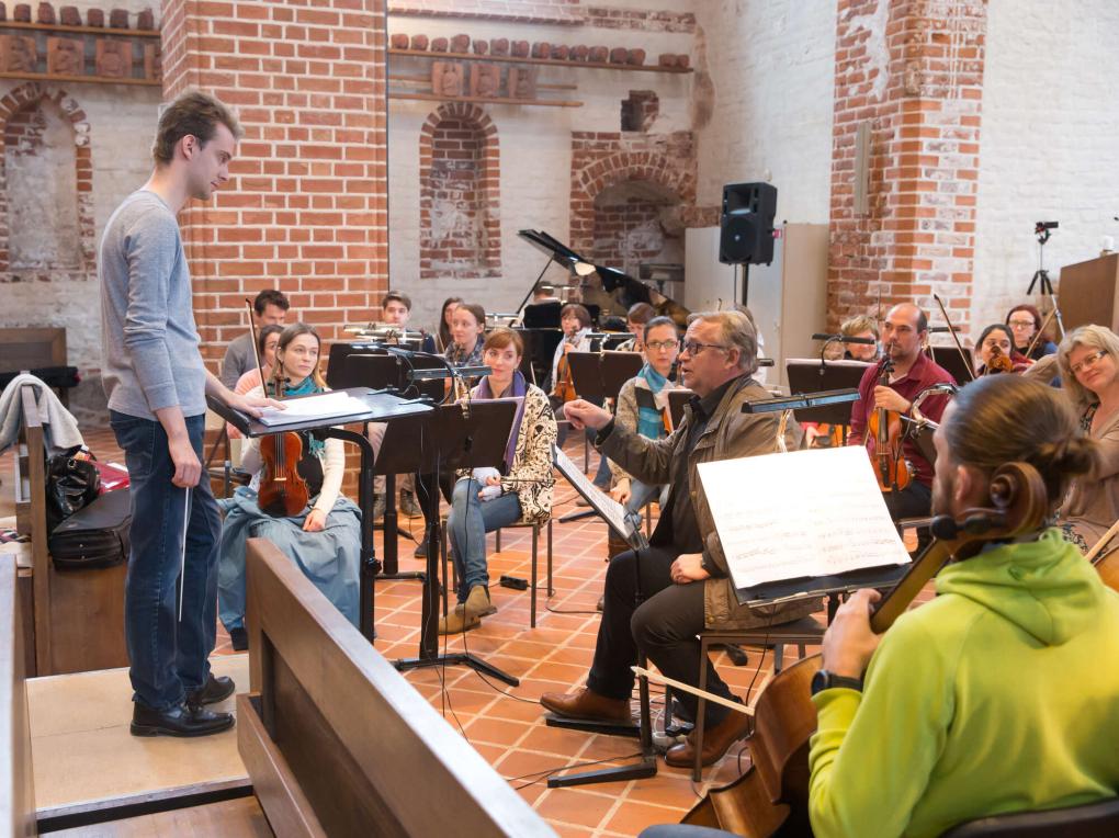 Junger Dirigent steht vor Orchester in Kirchenraum