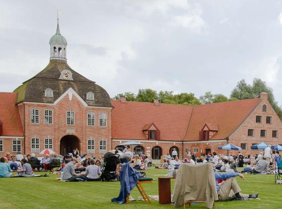 Menschen mit Campingstühlen und Sonnenschirmen vor Schloss mit roten Klinkermauern