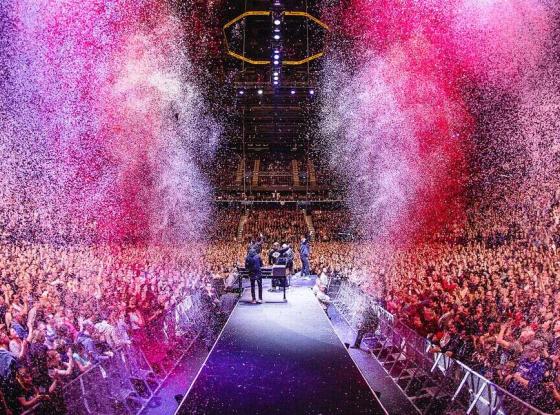 Die Hip-Hop-BAnd Die Fantastischen Vier stehen auf der Bühne, mit den Gesichtern zu einem riesigen Publikum. Links und rechts von der Bühne schießt rosafarbenes Confetti in die Höhe.