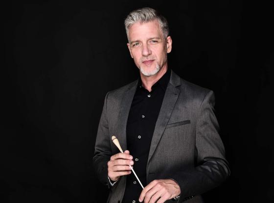 Porträt eines Herren im Jackett mit Dirigierstock vor dunklem Hintergrund