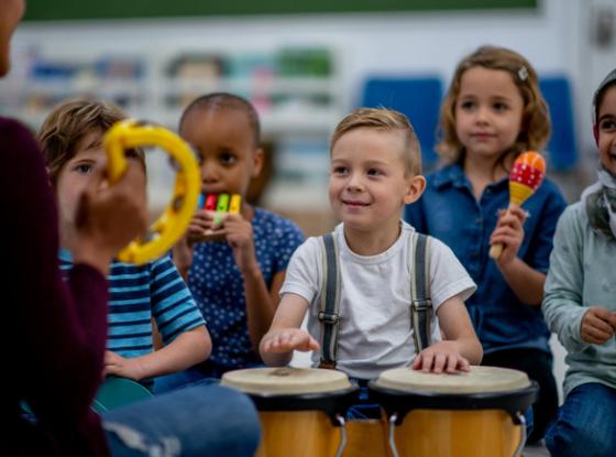 Kinder mit Rhythmusinstrumenten musizieren mit Musikpädagogin